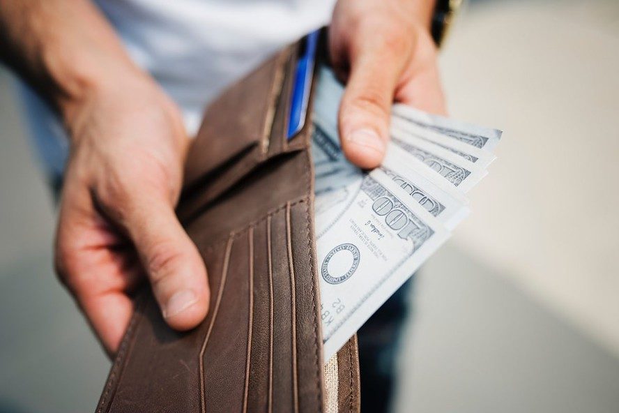 A man holding a brown wallet showing the cash he made from selling a house for cash.