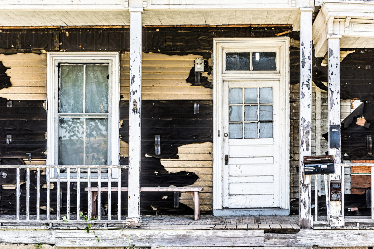 Old abandoned weathered wooden house with porch entrance, peeling paint, dirty windows