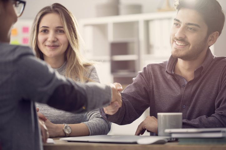 Young couple shaking hands with a person who buys houses for cash in Kansas City.