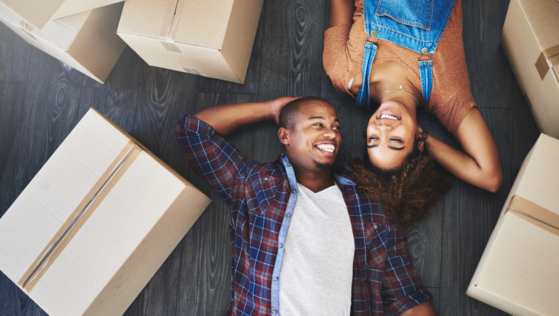 A young couple laying by moving boxes who is going to sell their house to cash buyers.